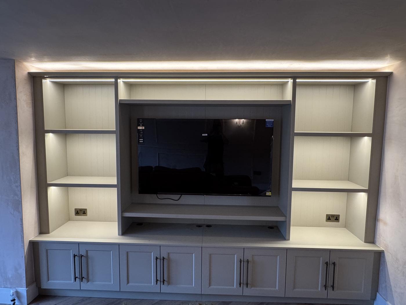 Grey media wall with lit shelving either side of a TV recess and shaker cupboards below