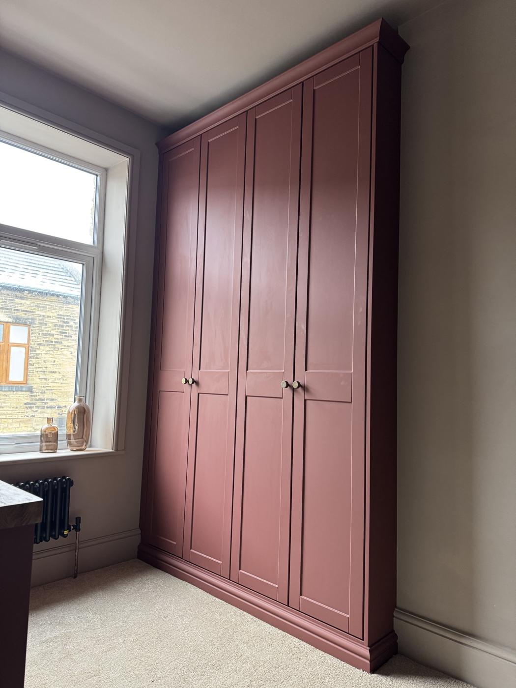Terracotta painted fitted wardrobes running floor to ceiling beside a window